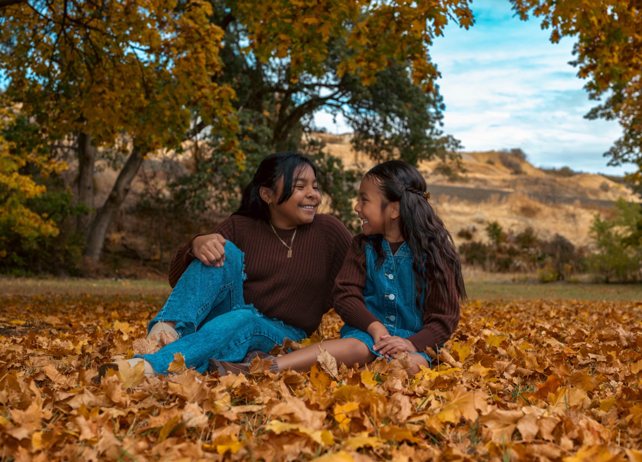 Two girls laughing together while sitting in autumn leaves