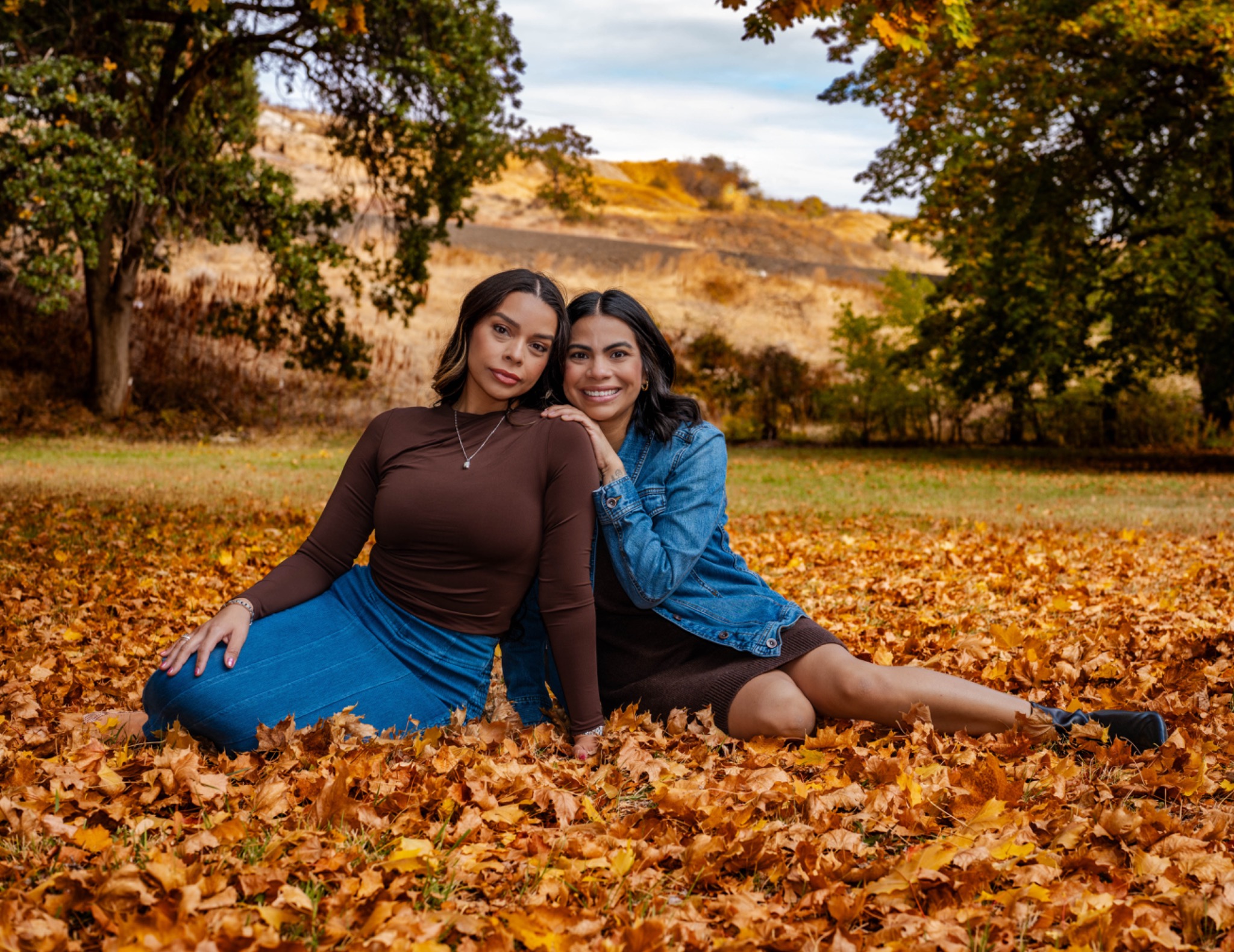 Two women sitting together among golden autumn leaves
