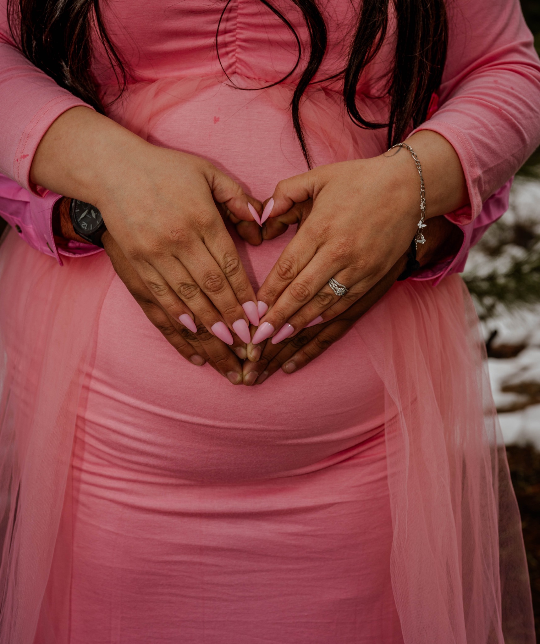 The couple’s hands form a heart over a pink maternity dress