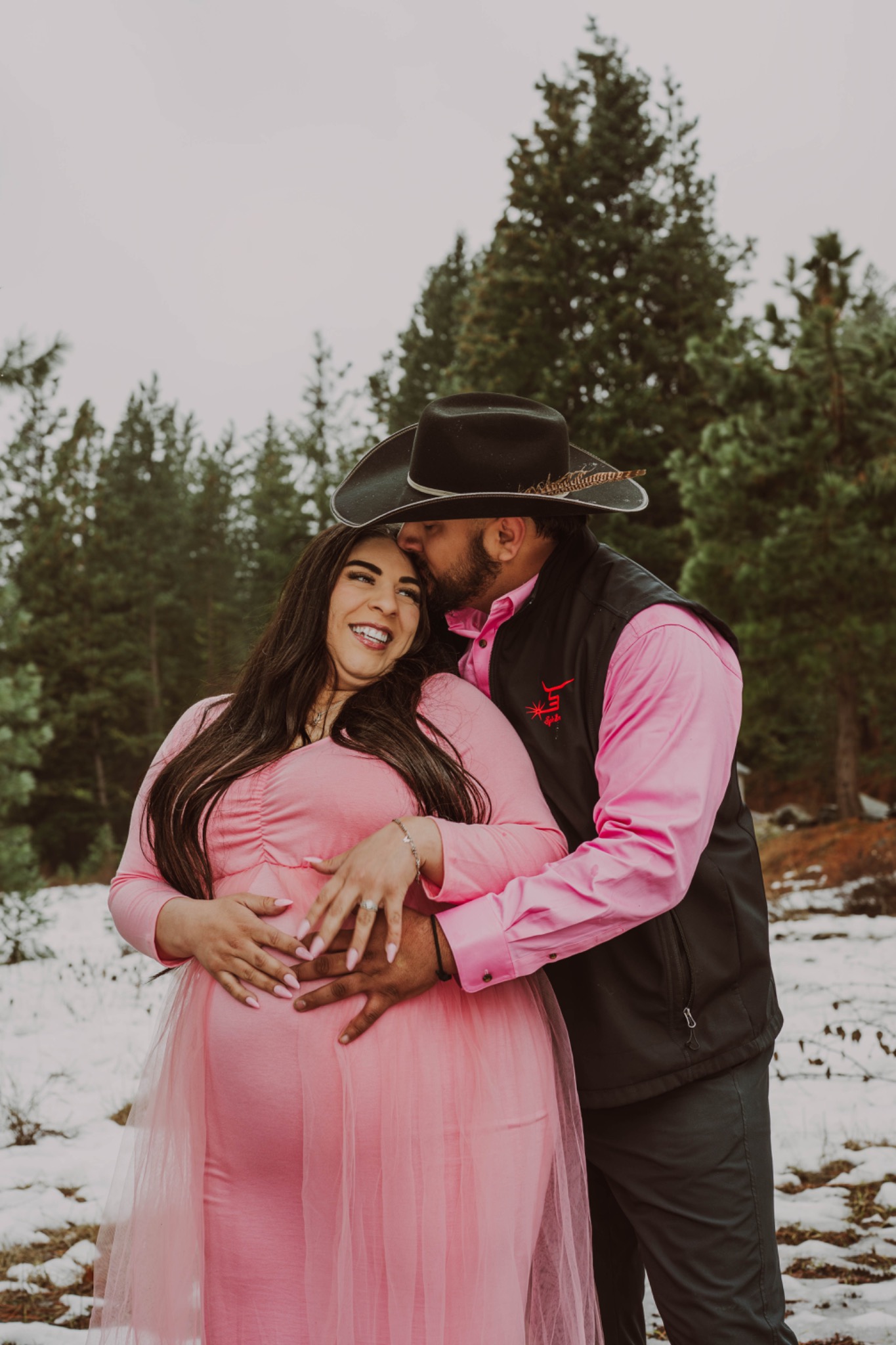 A couple sharing a joyful moment during a maternity session in the snowy woods