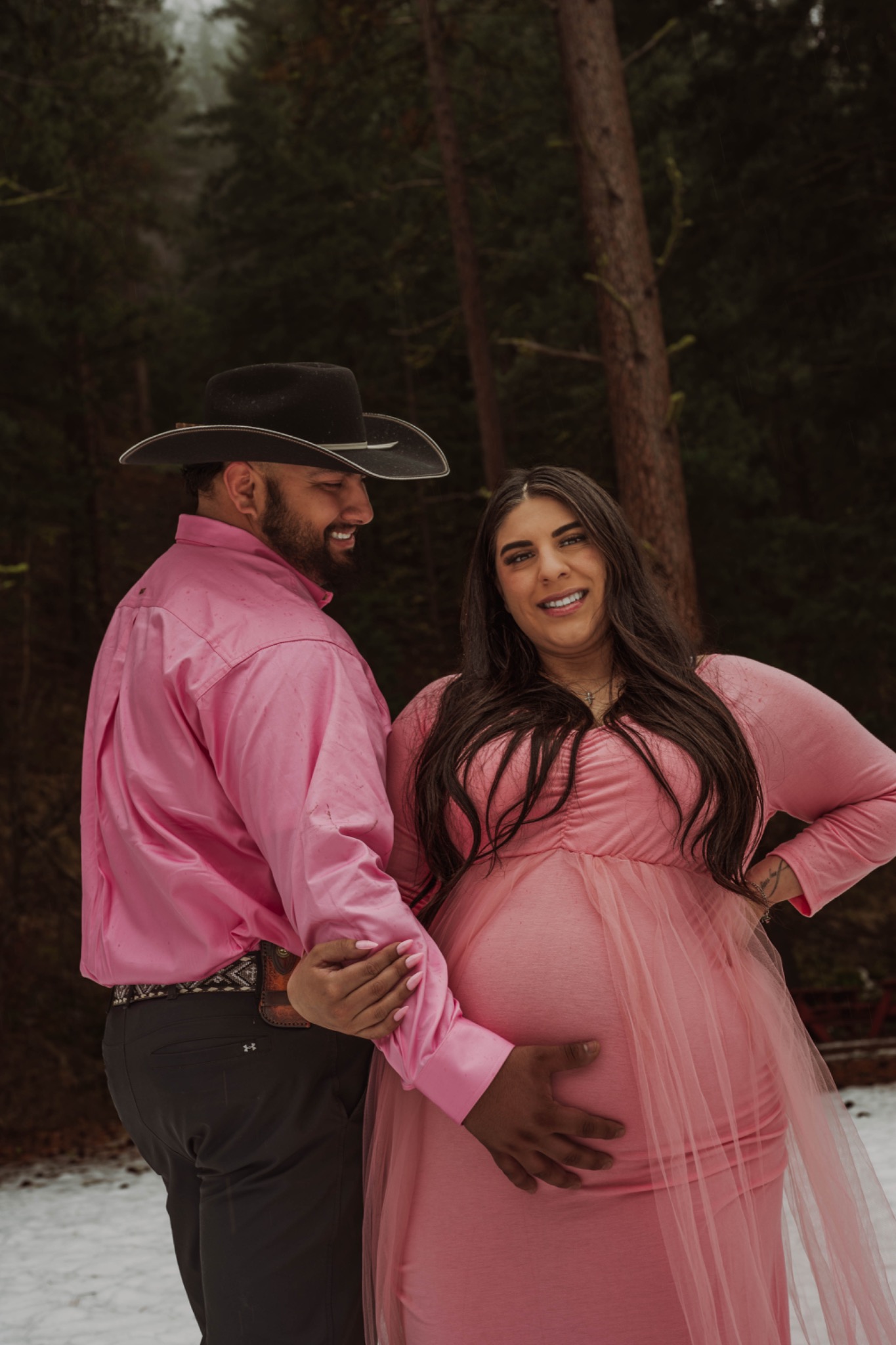 Expectant couple in coordinating pink outfits smiling in a wooded setting