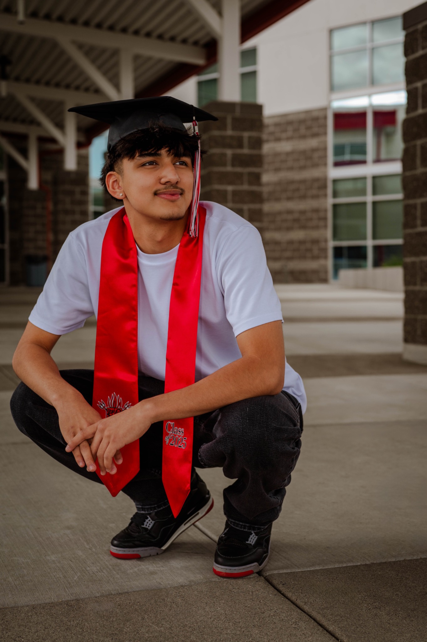 Senior graduate in a black cap and red stole seated outside his school