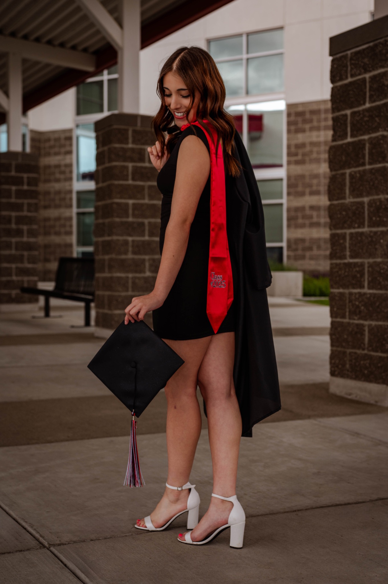 Smiling graduate in a black dress and red stole holding her graduation cap