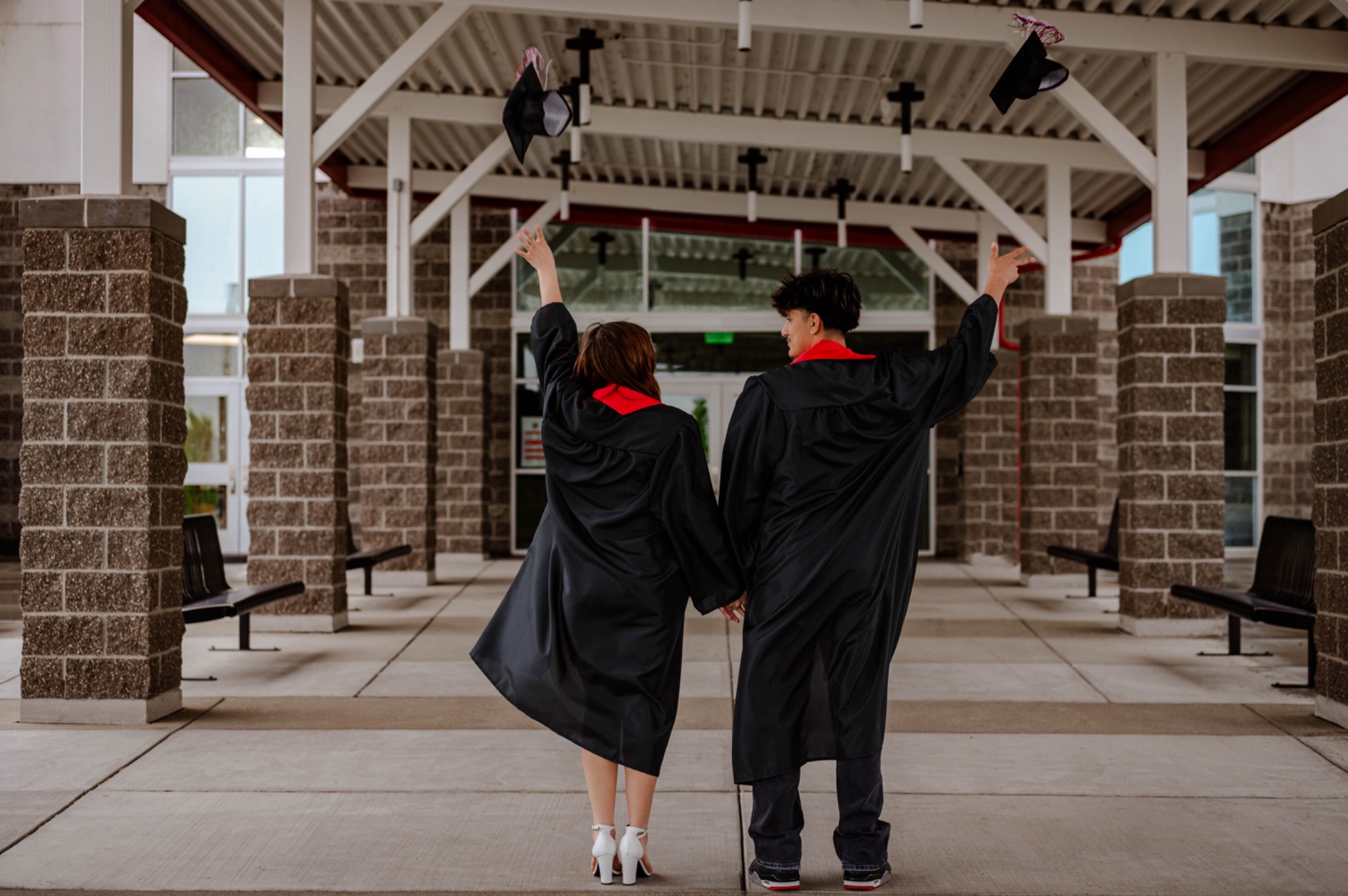 Two graduates throwing their caps into the air outside their school